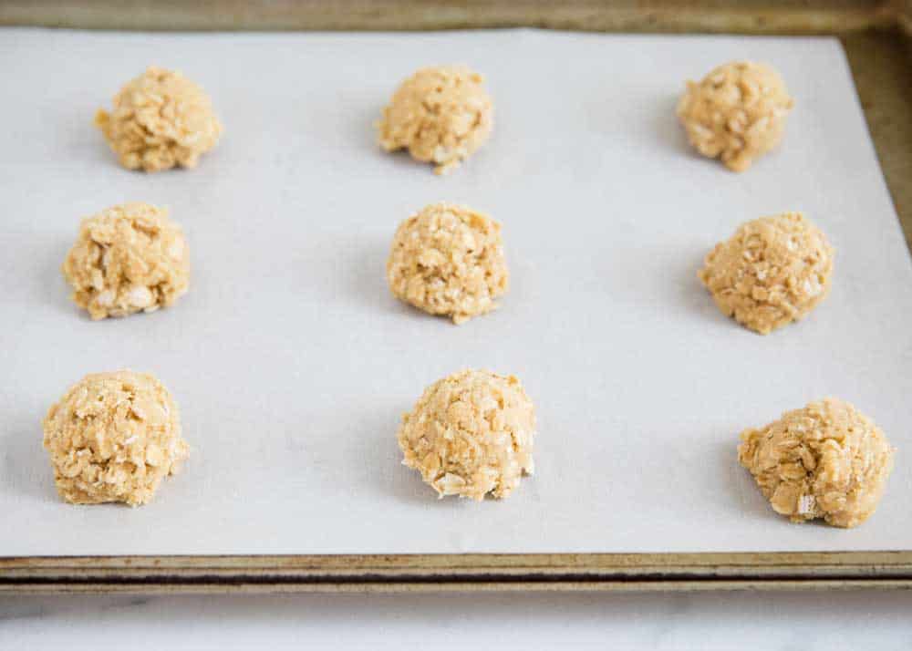 Oatmeal cookie dough balls on lined baking sheet.