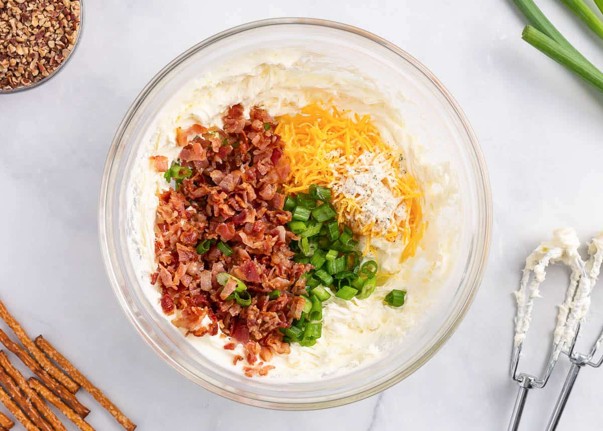 A glass bowl with cream cheese, cheese, ranch mix, green onions and bacon.