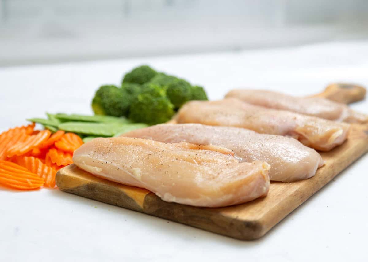 Chicken breasts on cutting board with stir fry veggie nearby.