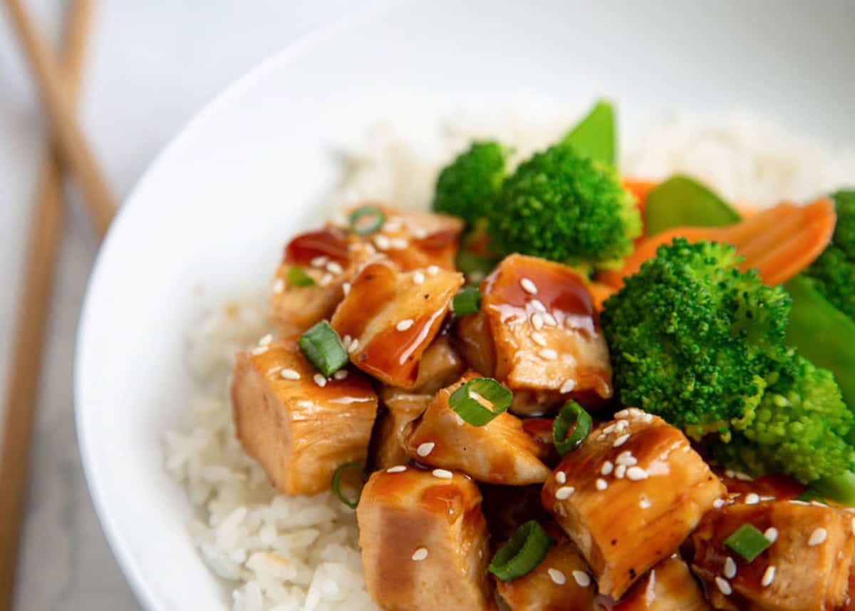 Teriyaki chicken bowl with rice and stir fry veggies in a white bowl.