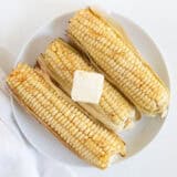 Grilled corn on the cob on a plate with a pat of butter.