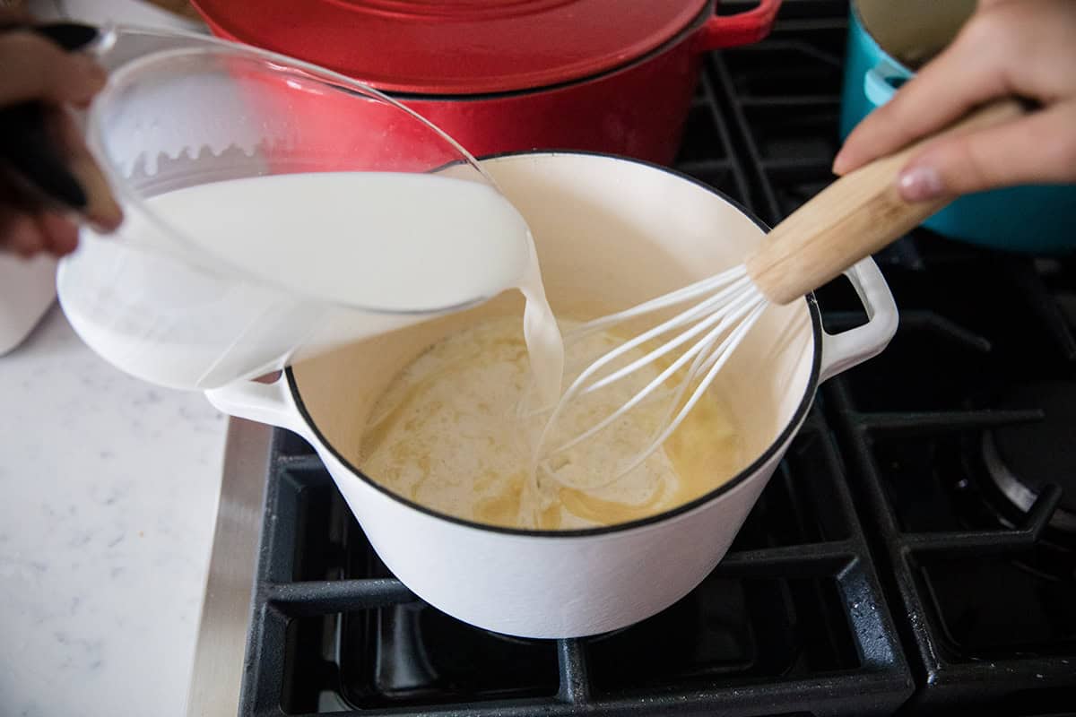 Whisking milk into a roux in a pot on the stove.