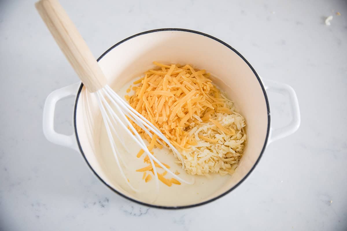 Adding cheese to milk in a white pot.