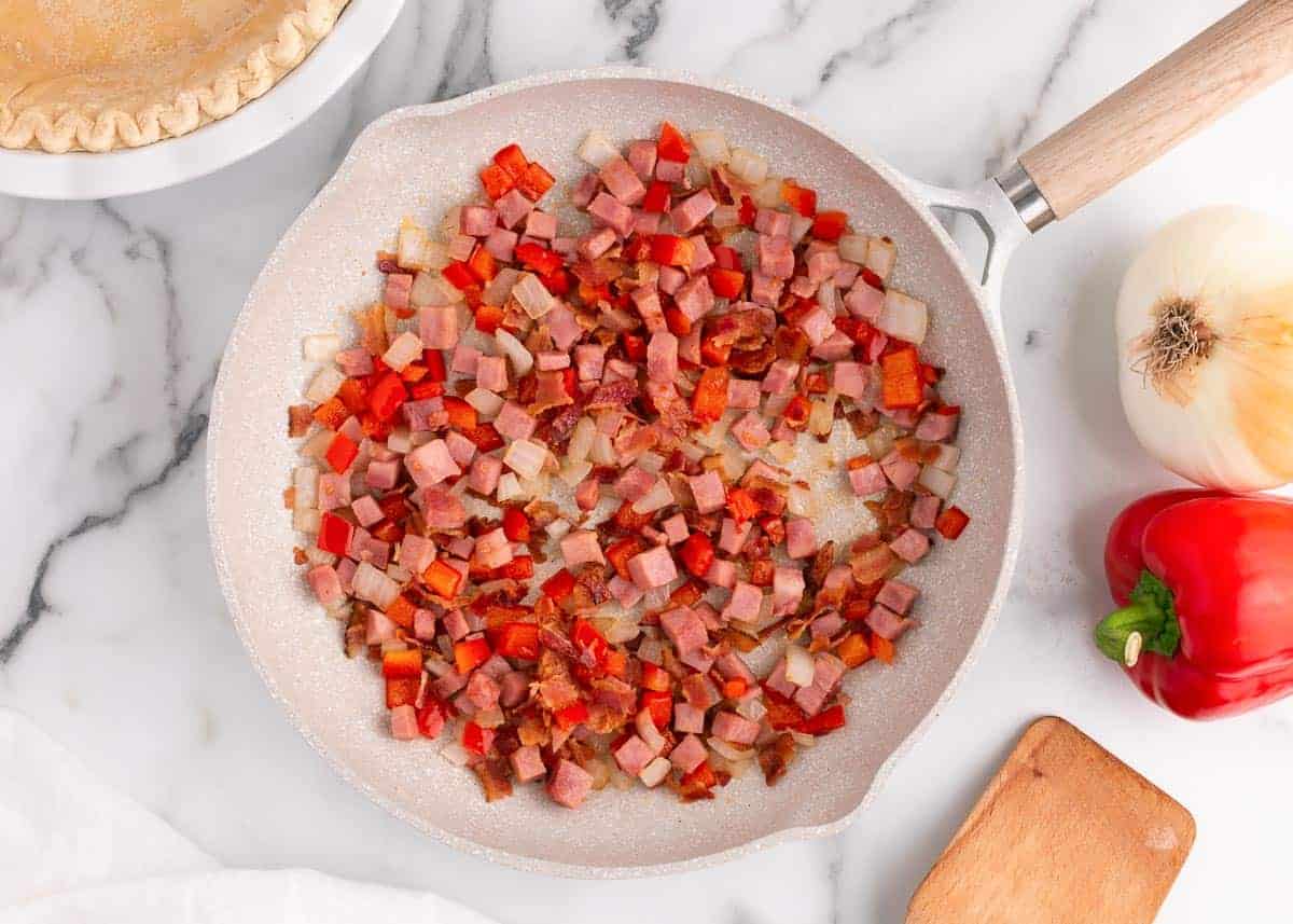 Onion, ham and bacon in a frying pan.