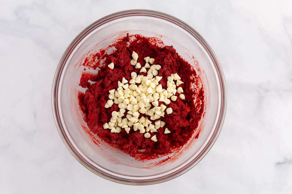 Red velvet cake mix cookie batter and white chocolate chips in a bowl.