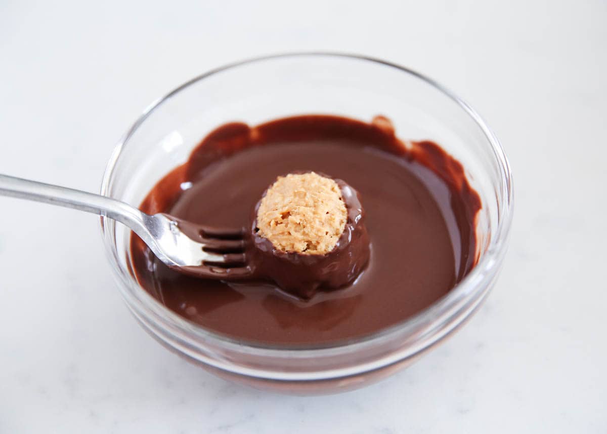 Dipping peanut butter rice krispie ball into melted chocolate.