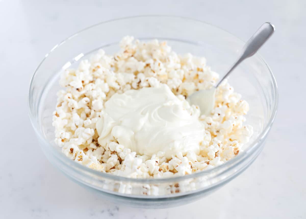 White chocolate being stirred into popcorn in a bowl.