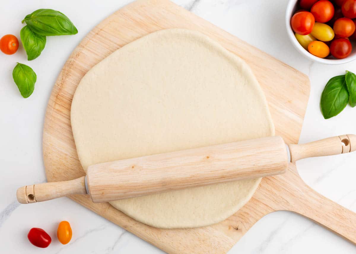 Rolling out pizza dough on wooden pizza peel.