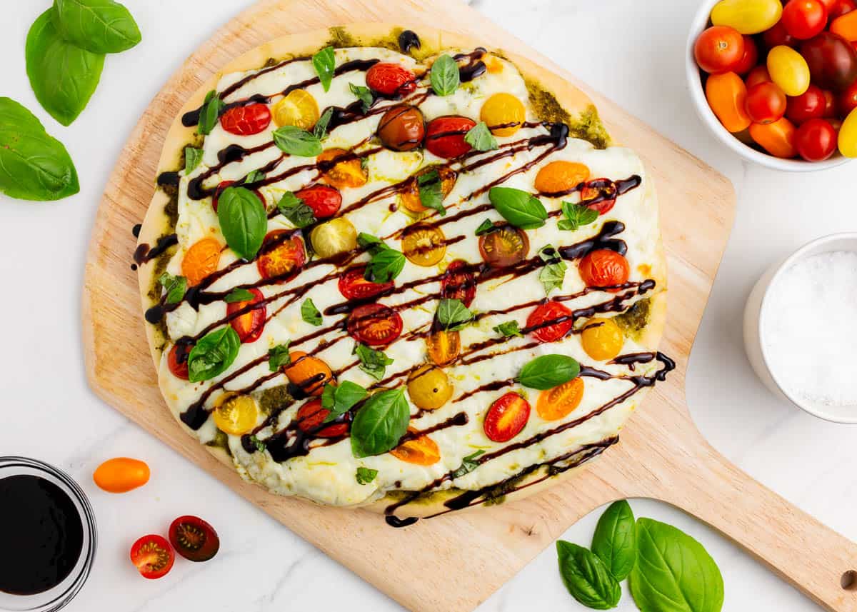 Caprese pizza on pizza peel drizzled with balsamic glaze.