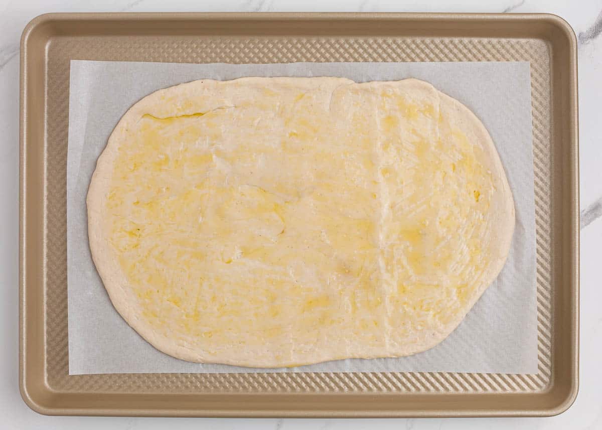 Pizza dough and olive oil on baking sheet.