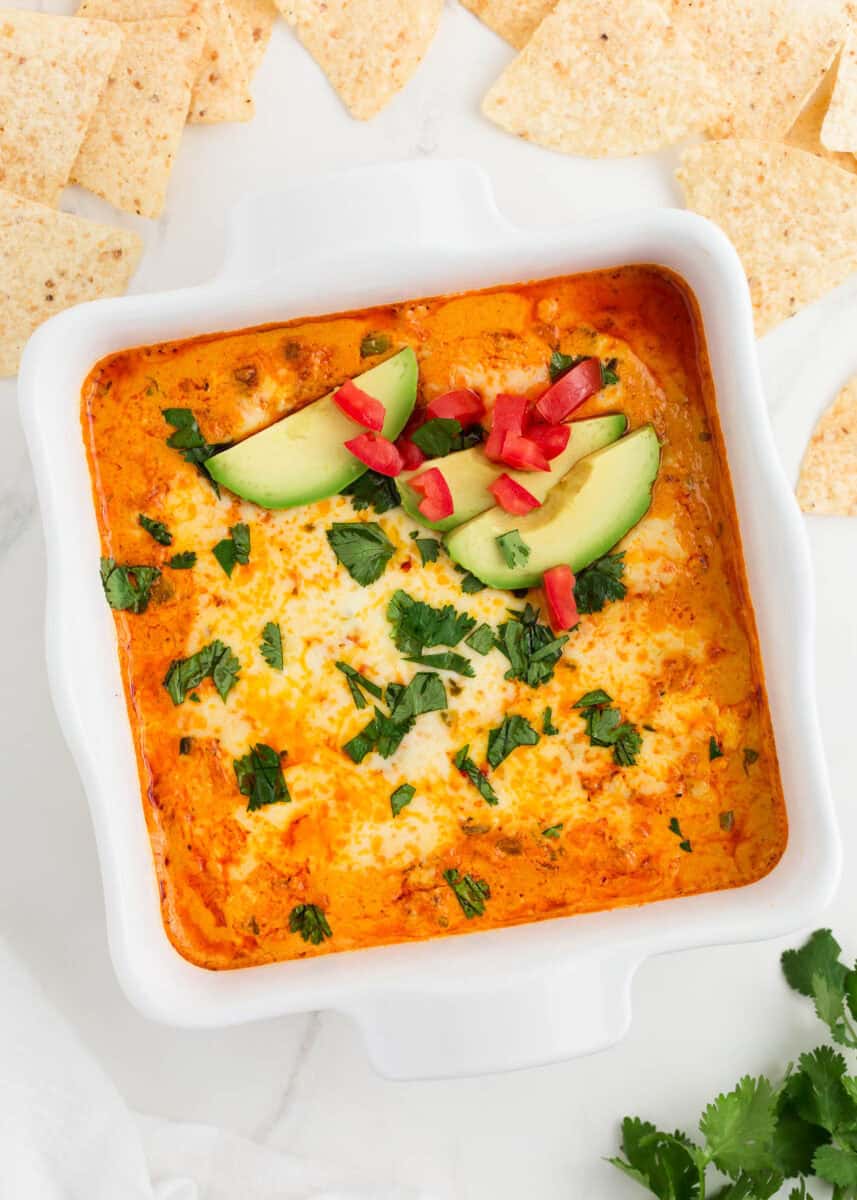 Chicken enchilada dip in a white baking dish with avocado and cilantro garnish.