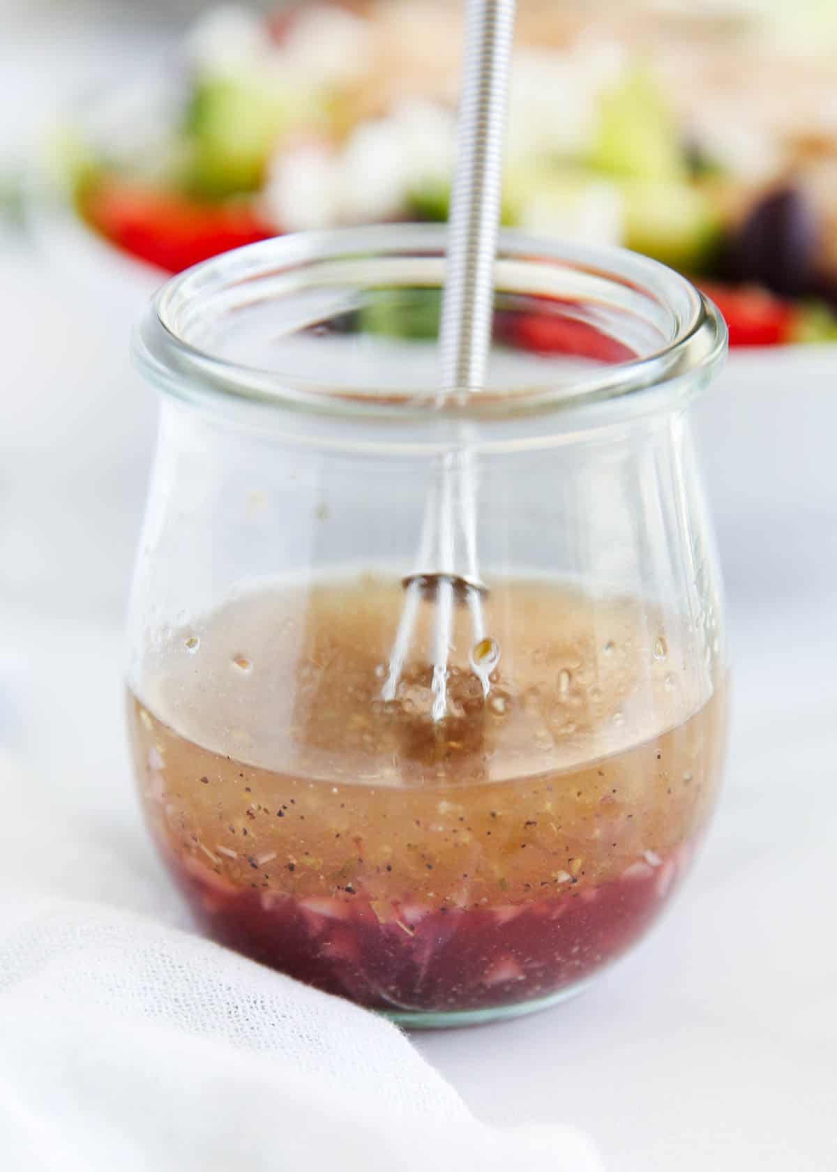 Greek salad dressing in a small glass jar with whisk.