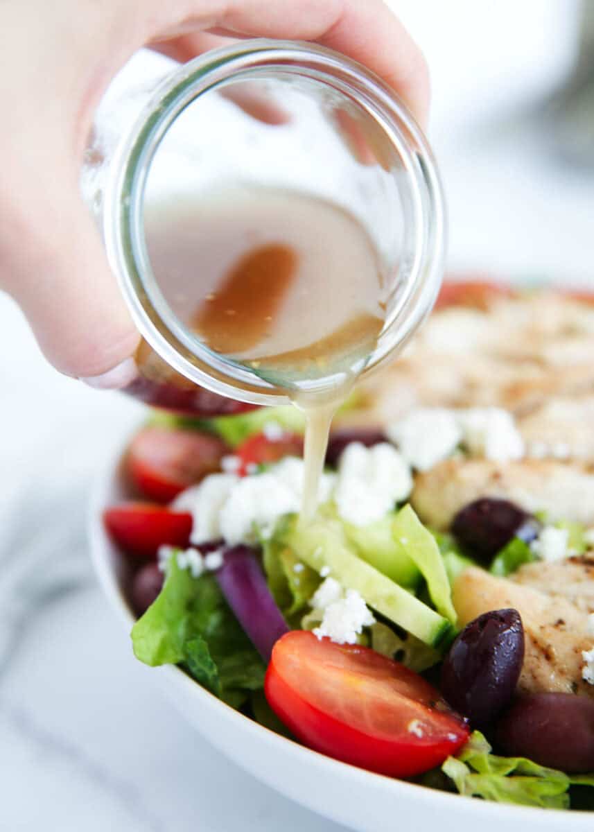 Greek salad dressing being drizzled over a salad.