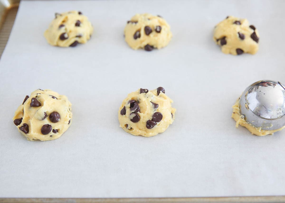 Scooping chocolate chip cookies from cake mix onto a parchment lined baking pan. 