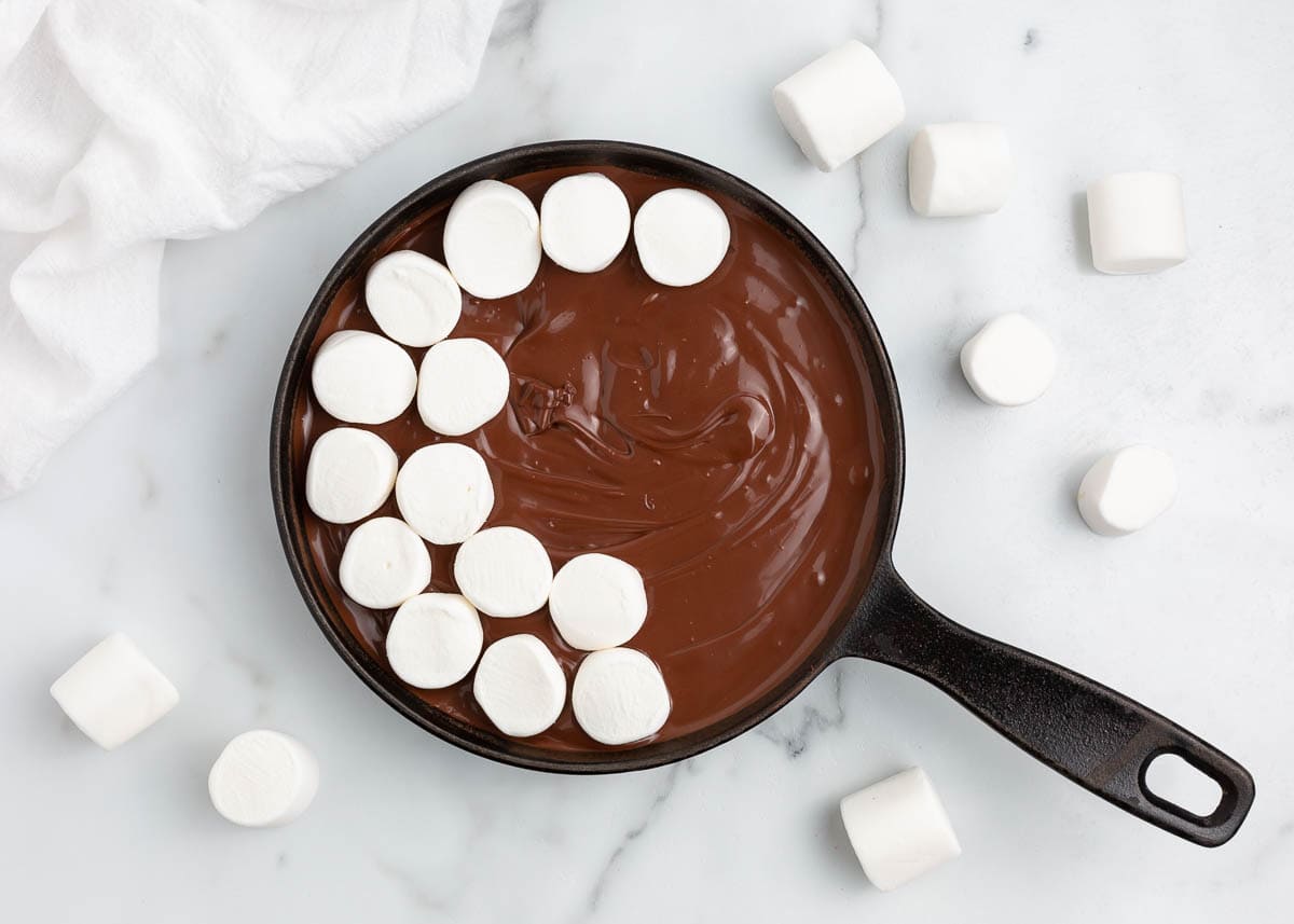 Marshmallows on top of melted chocolate in a cast iron skillet. 