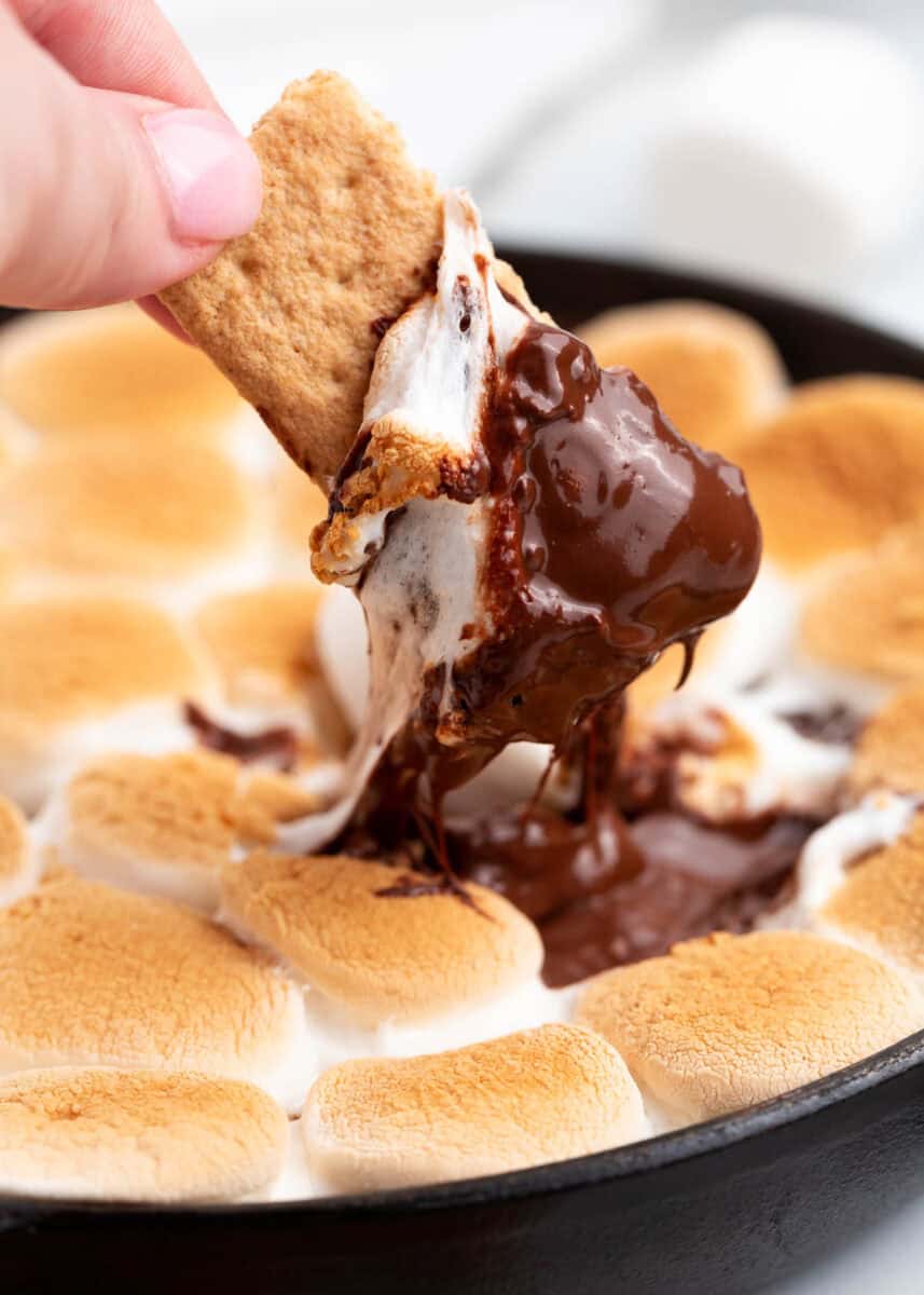 S'mores dip in a cast iron skillet with a graham cracker being dipped into it.