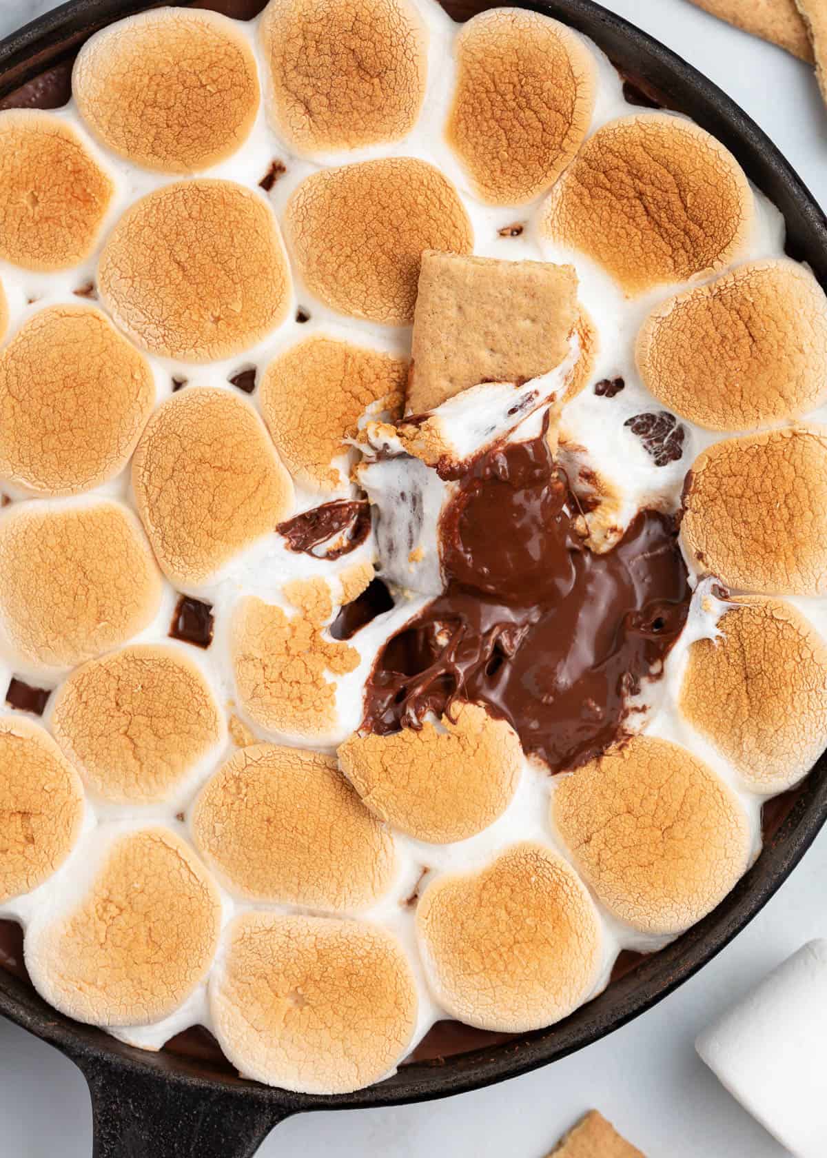 S'mores dip in a cast iron skillet with a graham cracker dipped into it.