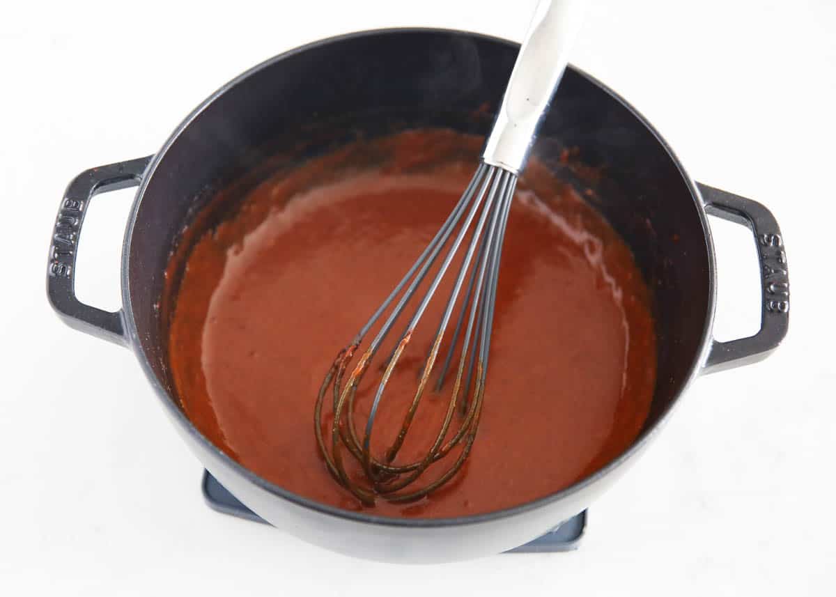 Enchilada sauce in a pan with a whisk.