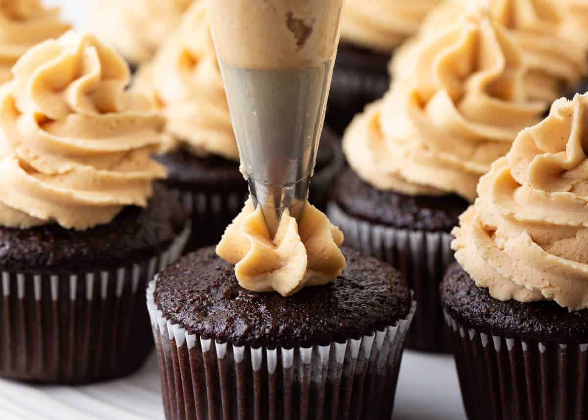 Piping peanut butter frosting on chocolate cupcakes.