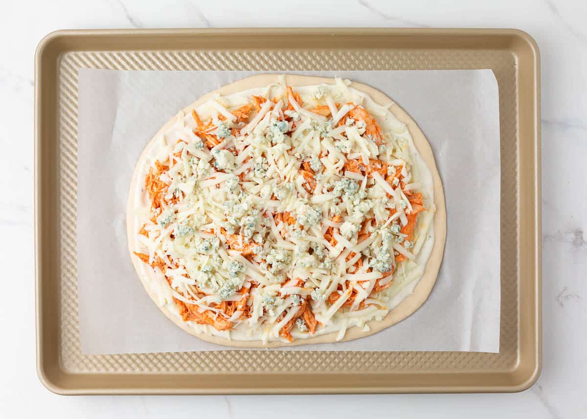 Bleu cheese and mozzarella on top of buffalo chicken on pizza dough.