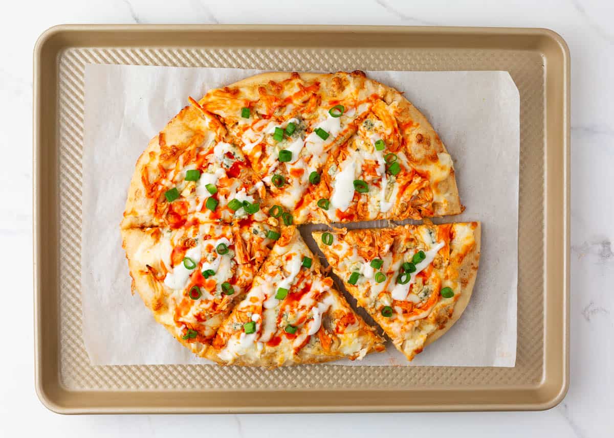 Sliced buffalo chicken pizza on baking sheet.