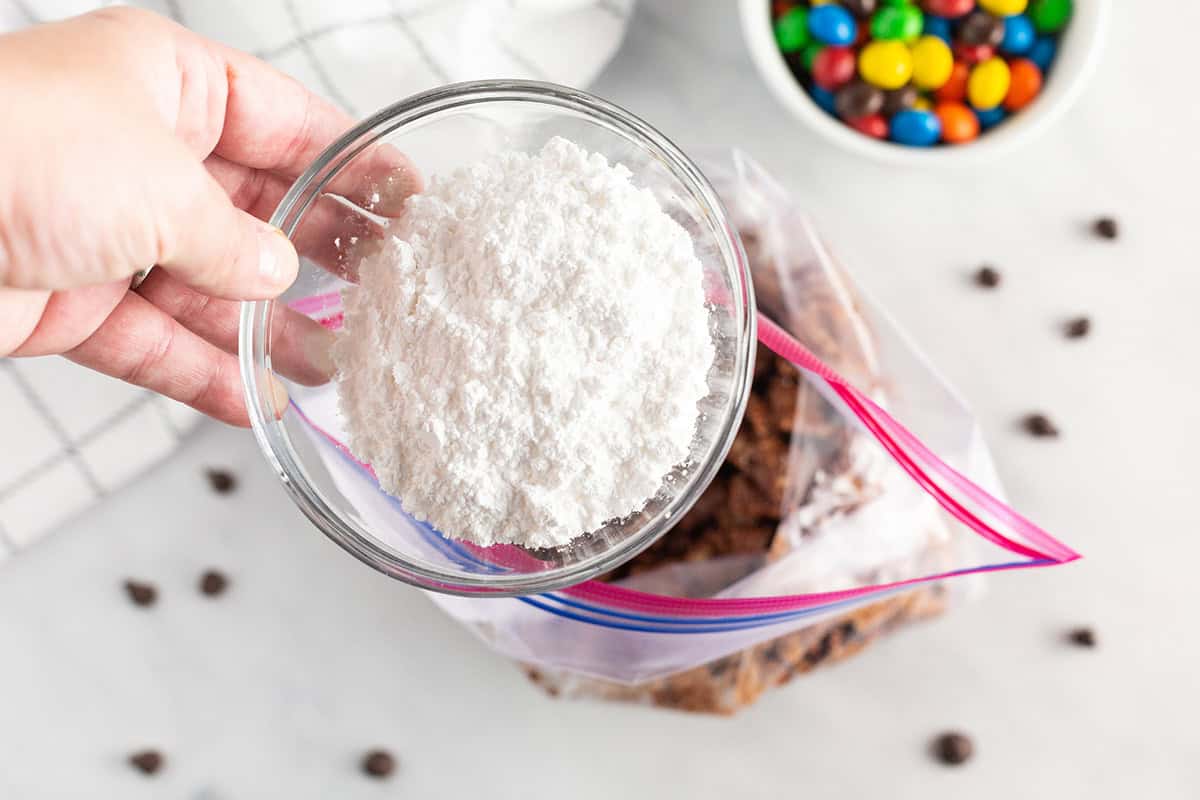 Powdered sugar being poured into a ziploc bag with Chex.