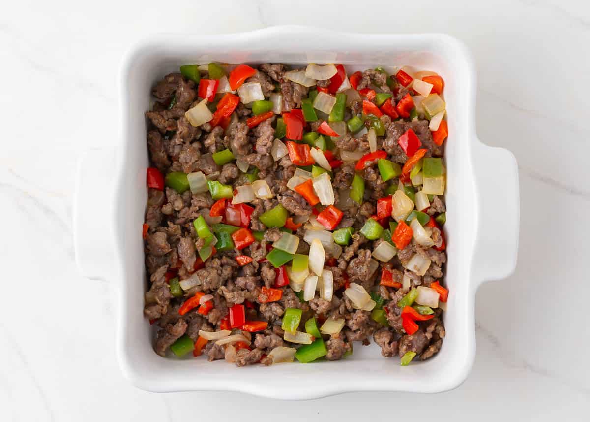 Cooked sausage, eggs and peppers in a white baking dish.