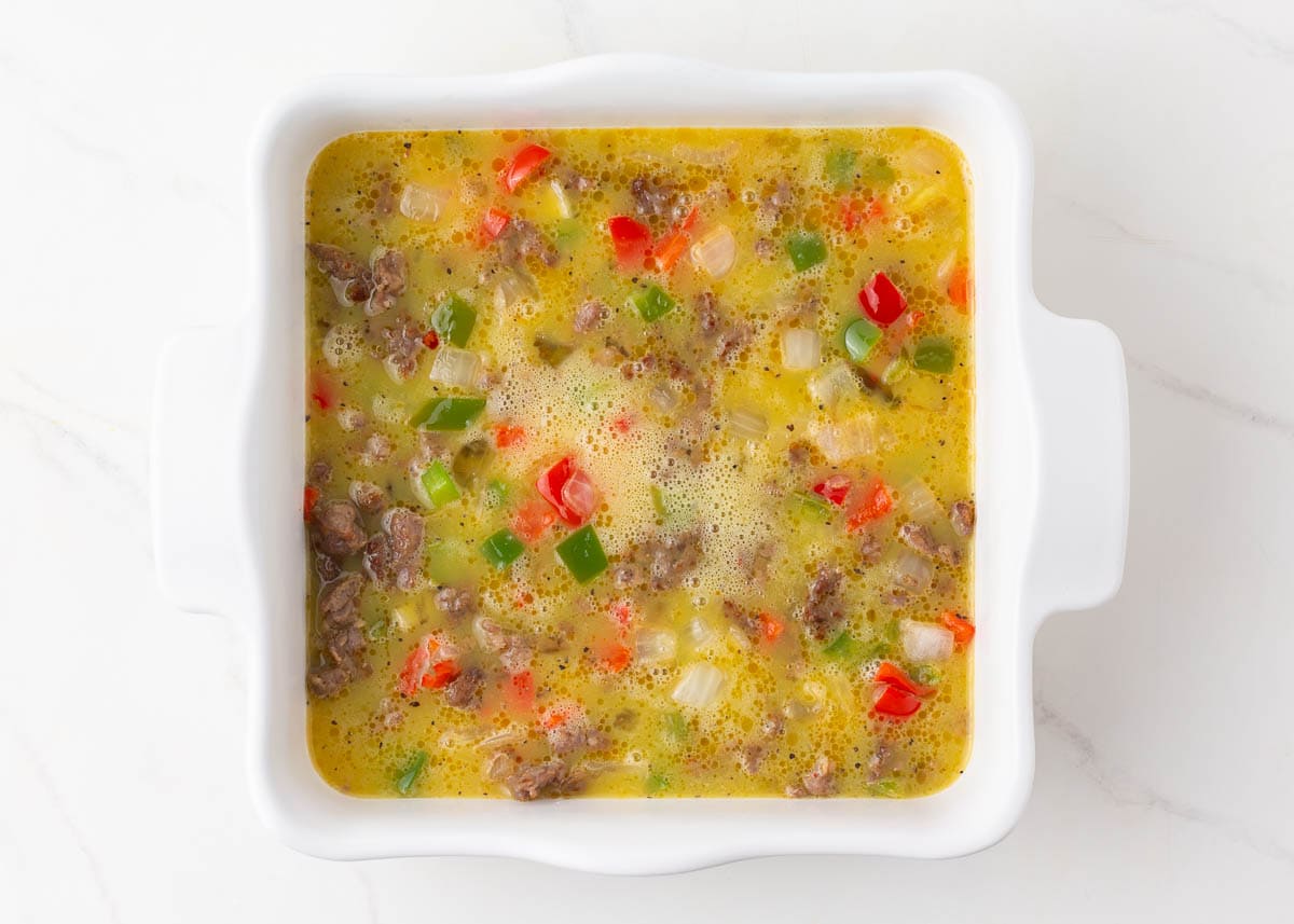 Egg mixture poured over sausage and peppers in a baking dish.