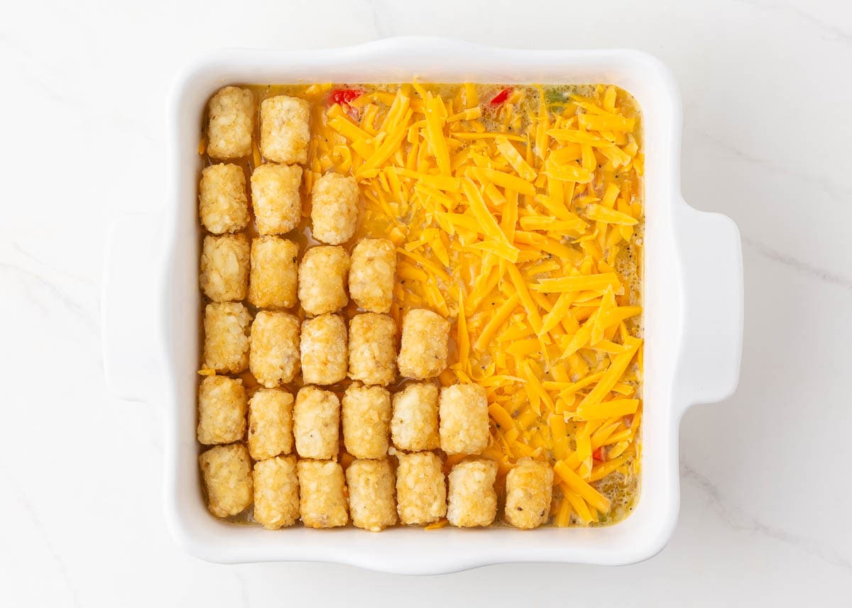 Tater tots and cheese over egg mixture in a casserole dish.