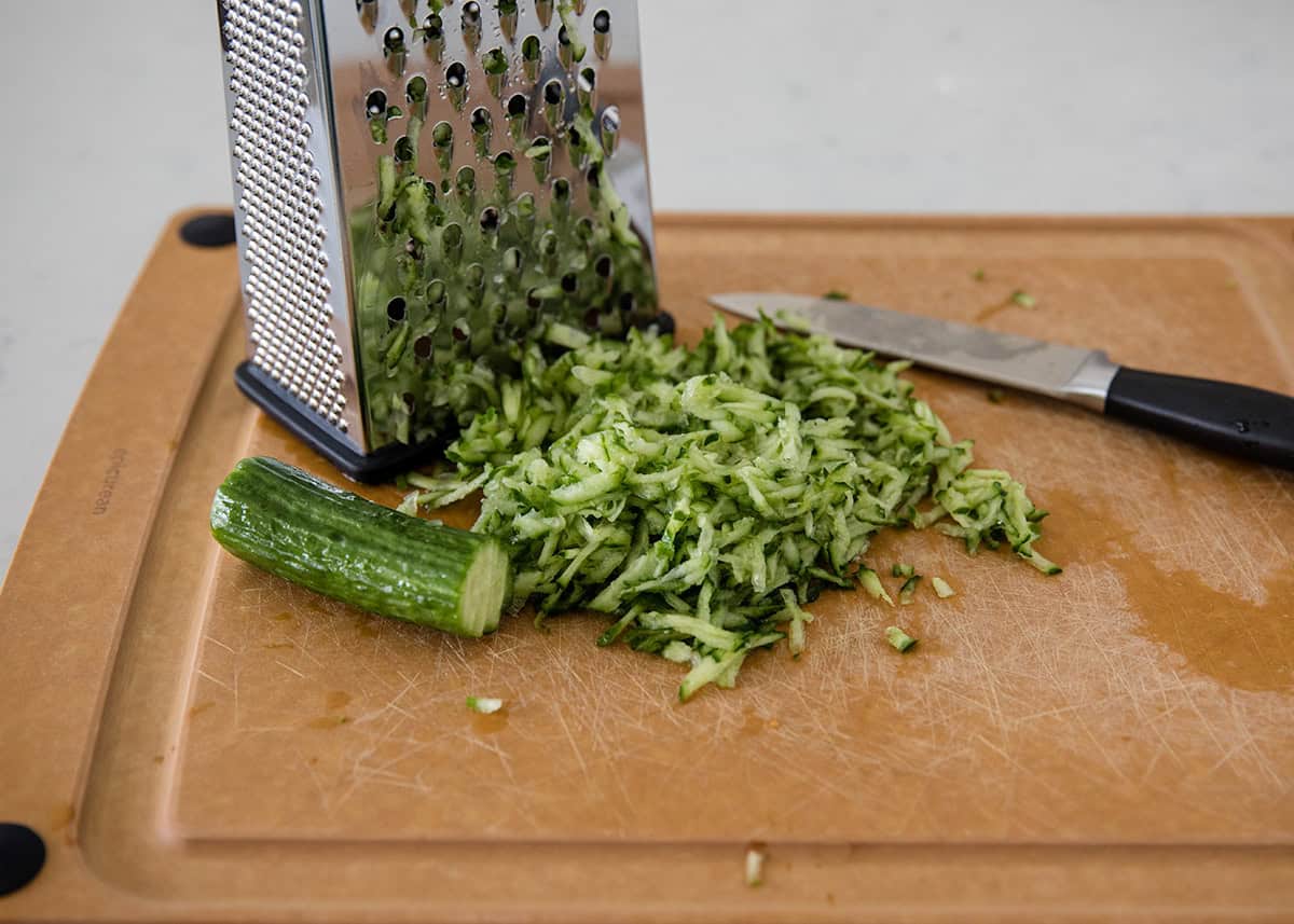 Cucumber grated with box grate on cutting board.