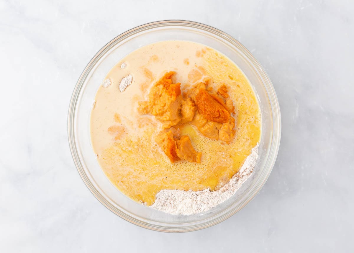 Flour, sugar, baking powder, pumpkin spice, cinnamon with pumpkin, milk and egg in a glass bowl.