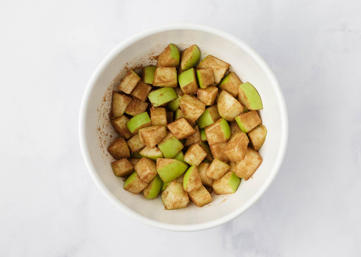 Cinnamon sugar and apples tossed in a bowl.