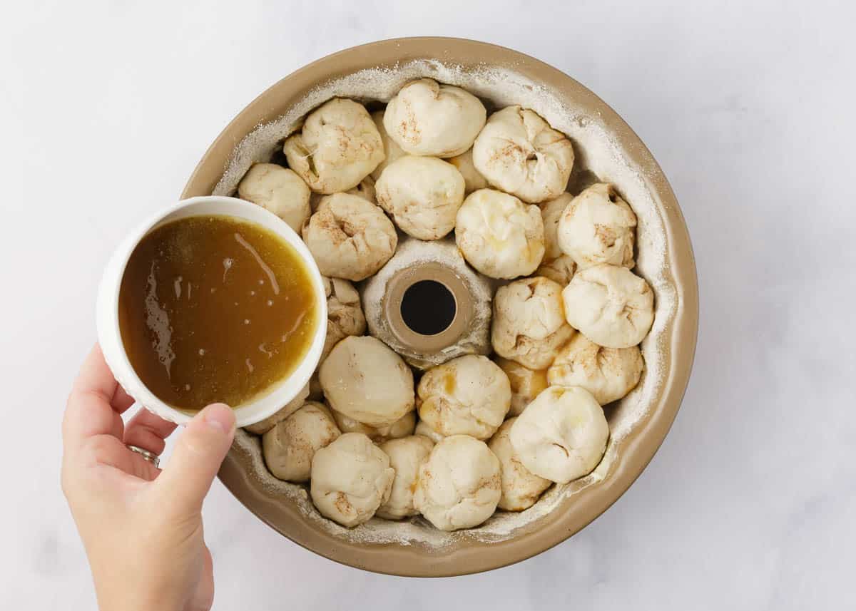 Caramel sauce poured over biscuit dough and apples in a bundt pan.