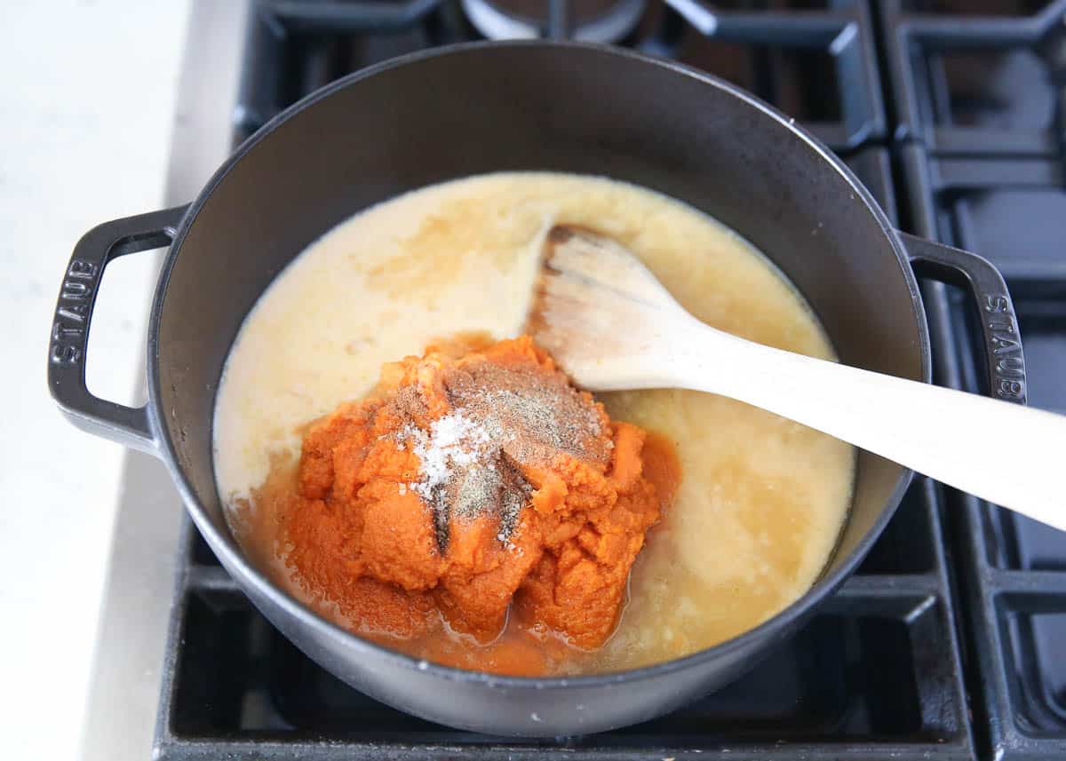 Adding pumpkin, coconut cream and broth to pot with warm spices.