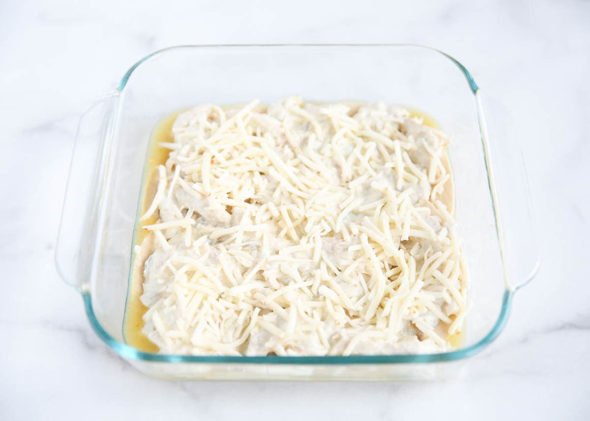 Cheese layered over tortillas with green enchilada sauce in a baking dish.