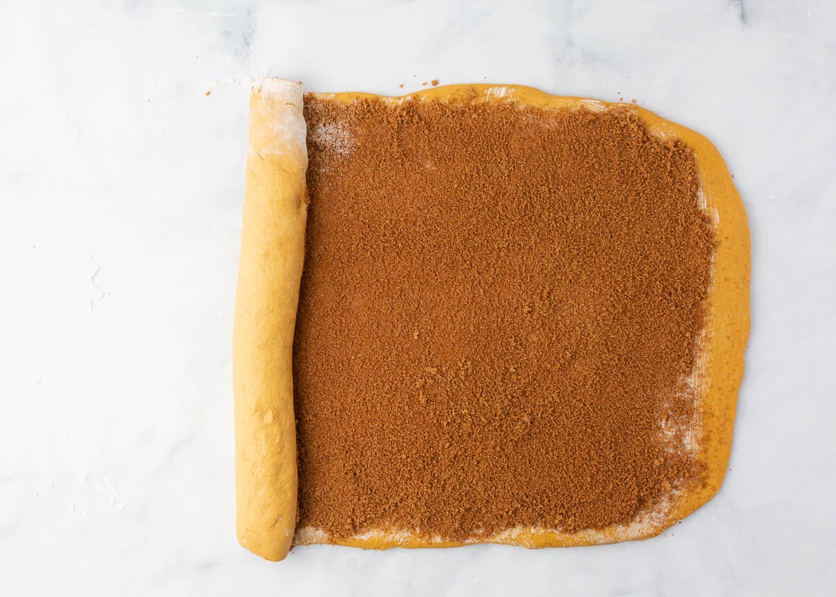 Pumpkin cinnamon roll dough rolled out and sprinkled with brown sugar pumpkin spice filling.