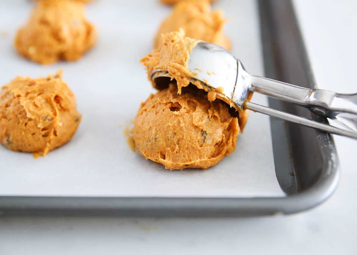 Pumpkin cake mix cookie batter being scooped onto a baking sheet.