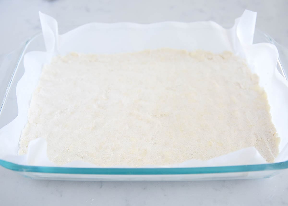 Shortbread crust in parchment paper lined baking dish.