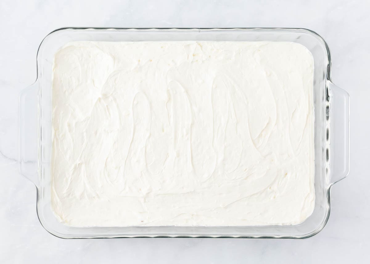 Cool whip cream cheese mixture layered on top of pretzel crust in a baking dish.