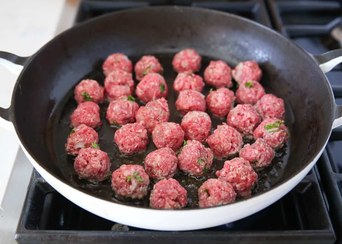 Meatballs browning in a skillet on the stove.