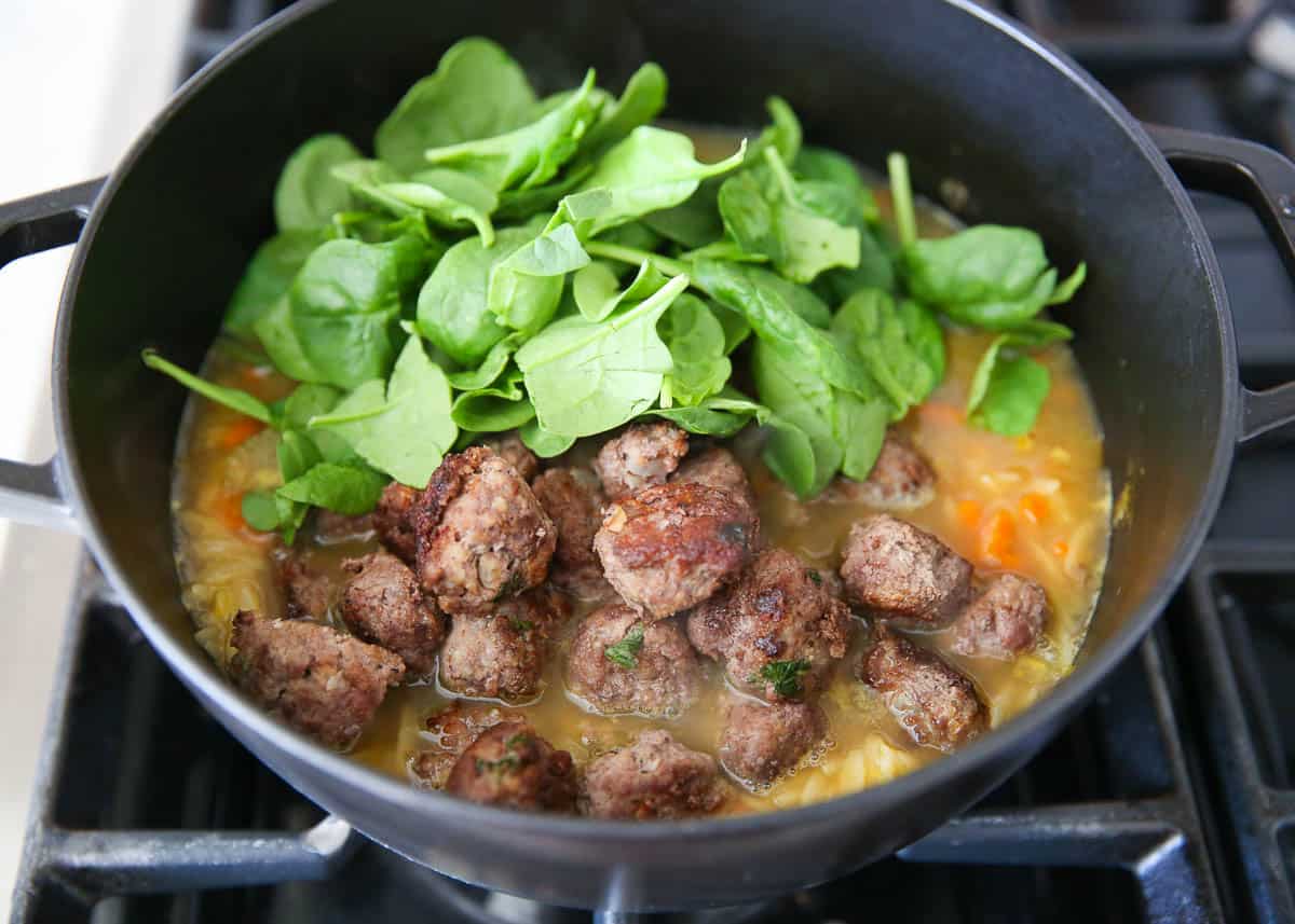 Meatballs, spinach, pasta and broth in a large pot for Italian wedding soup.