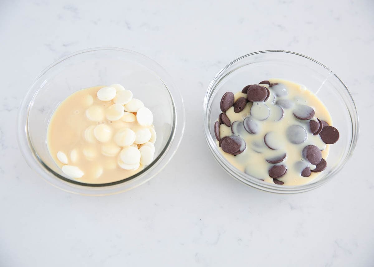 Sweetened condensed milk divided into bowls with chocolate melting wafers and white chocolate melting wafers.