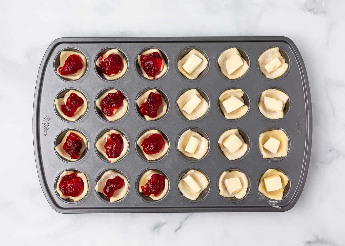 A muffin tin filled with brie and cranberry sauce.