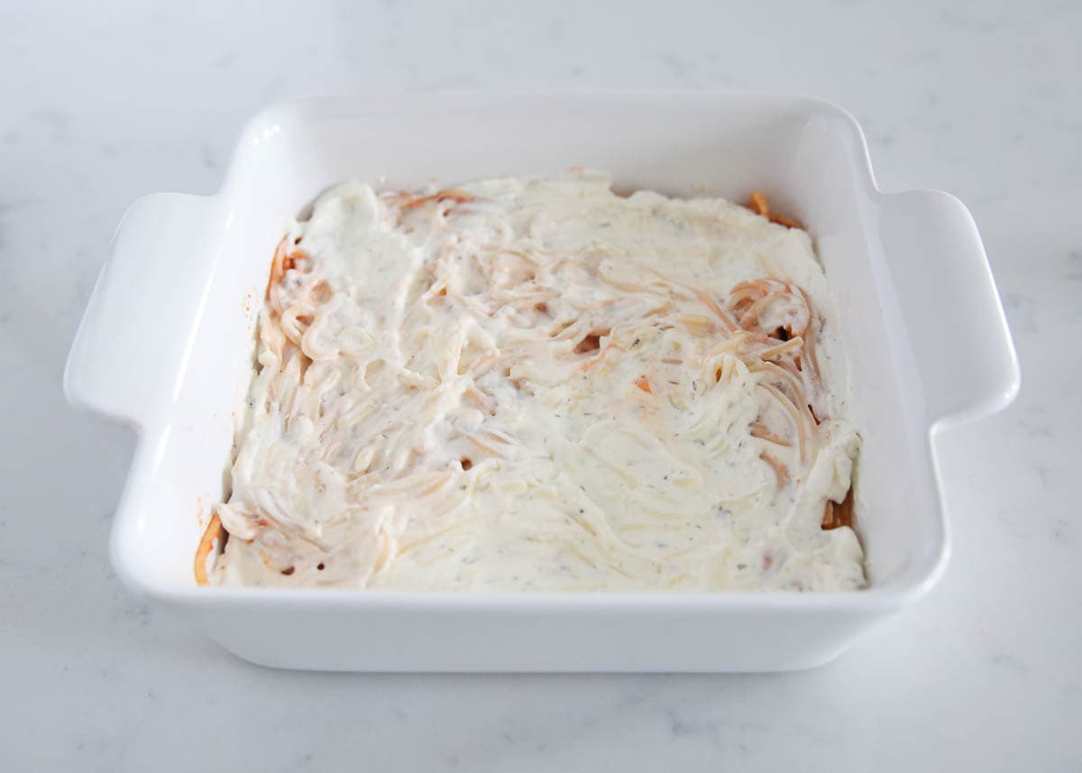 Ricotta mixture over top spaghetti in a baking dish.