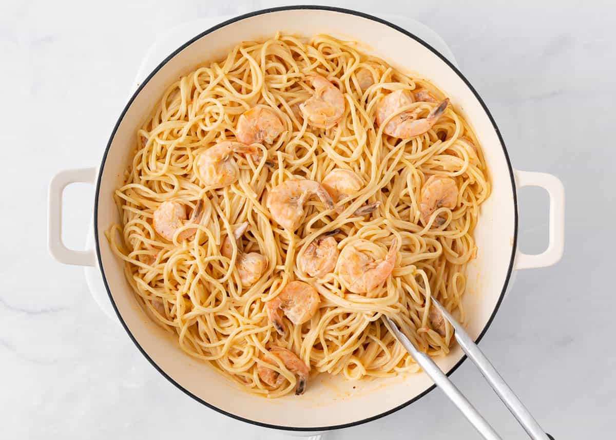 Bang bang shrimp with pasta being tossed together with tongs.