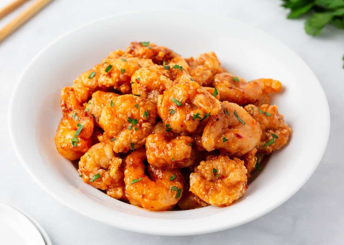 Shrimp tossed in bang bang sauce in a white bowl.