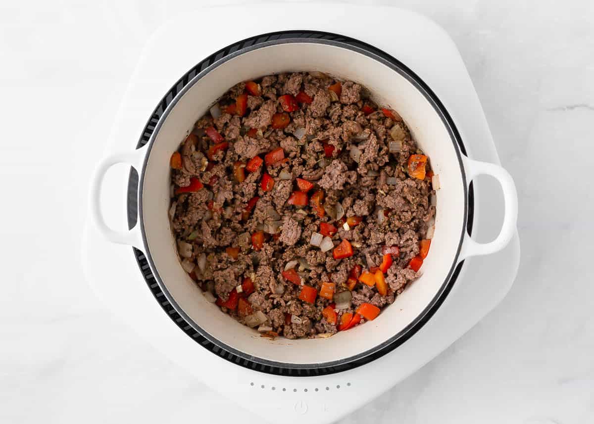 Ground beef, onion and pepper in a white pot.