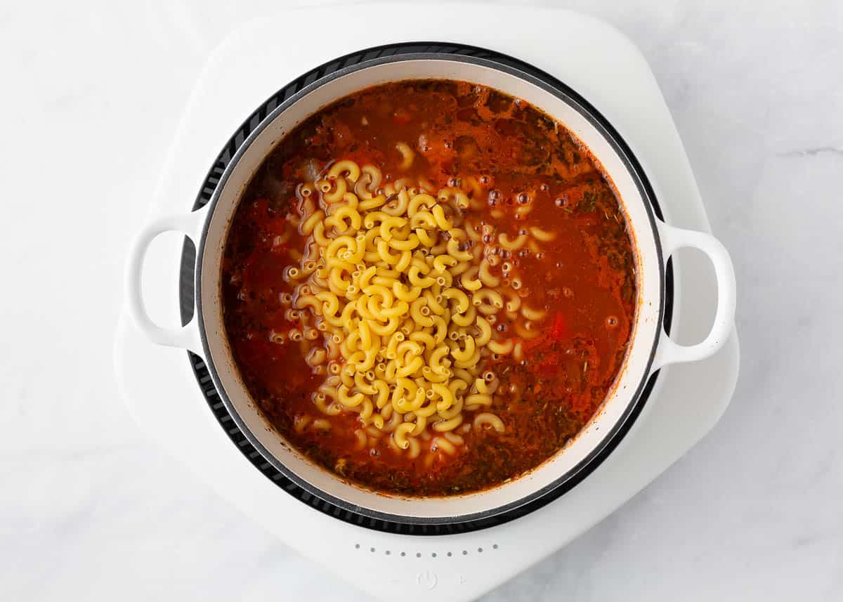 Elbow noodles and tomato sauce added to a pot containing beef and veggies.