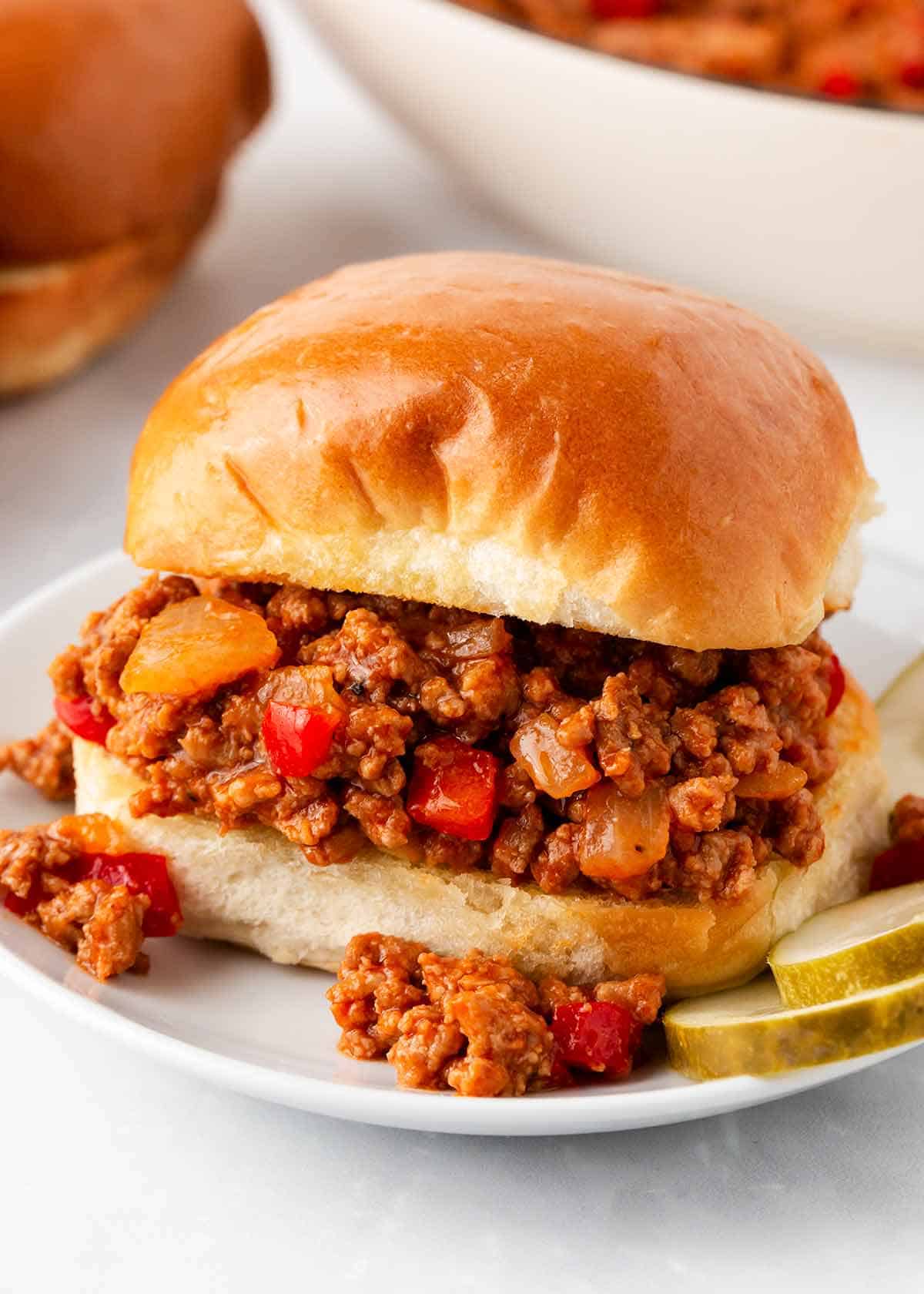 A turkey sloppy joe on a plate with pickles.