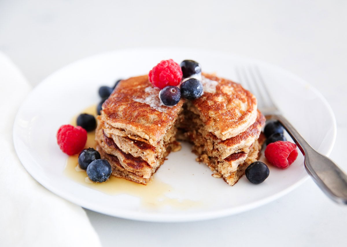 Cut blender oatmeal pancakes on a white plate with berries.